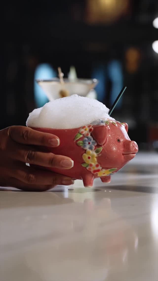 A pink ceramic pig mug full of foam, held over the bar